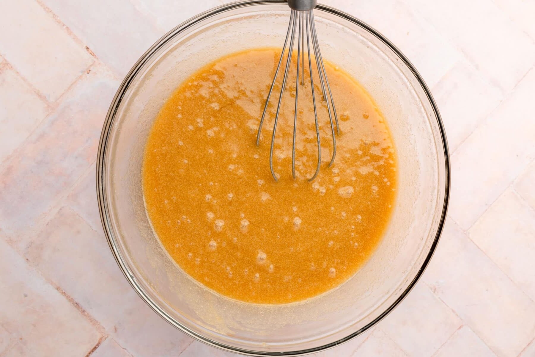 A glass mixing bowl with an orange sugar and melted butter mixture to make cookies.