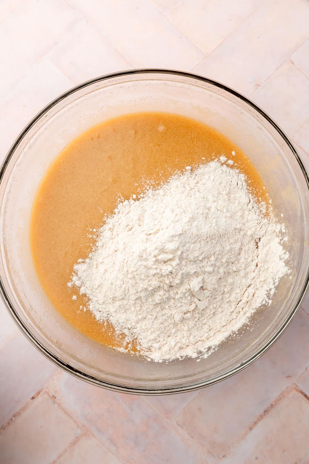 A glass mixing bowl with gluten-free flour on top of a melted butter and sugar mixture.