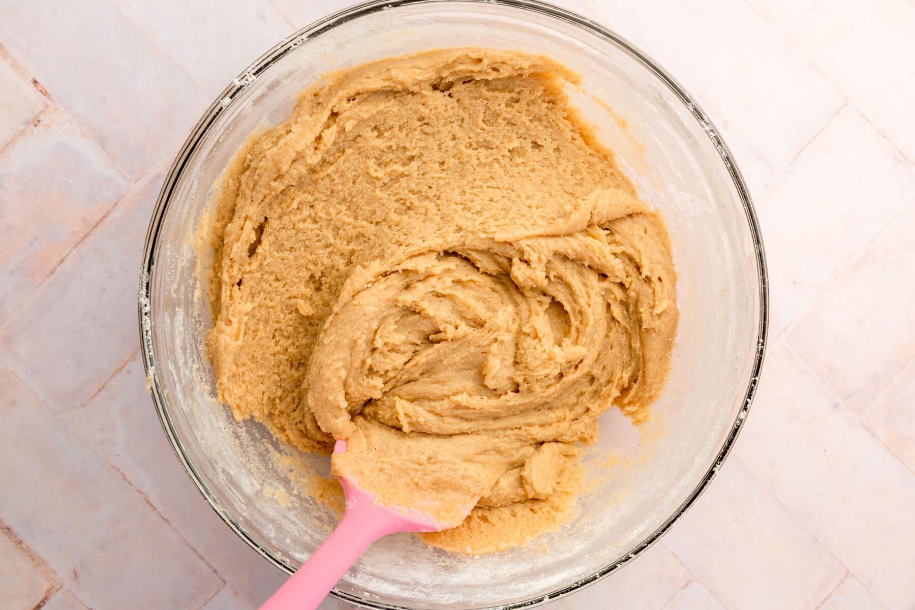 A bowl of gluten-free snickerdoodle cookie dough with a pink spatula.