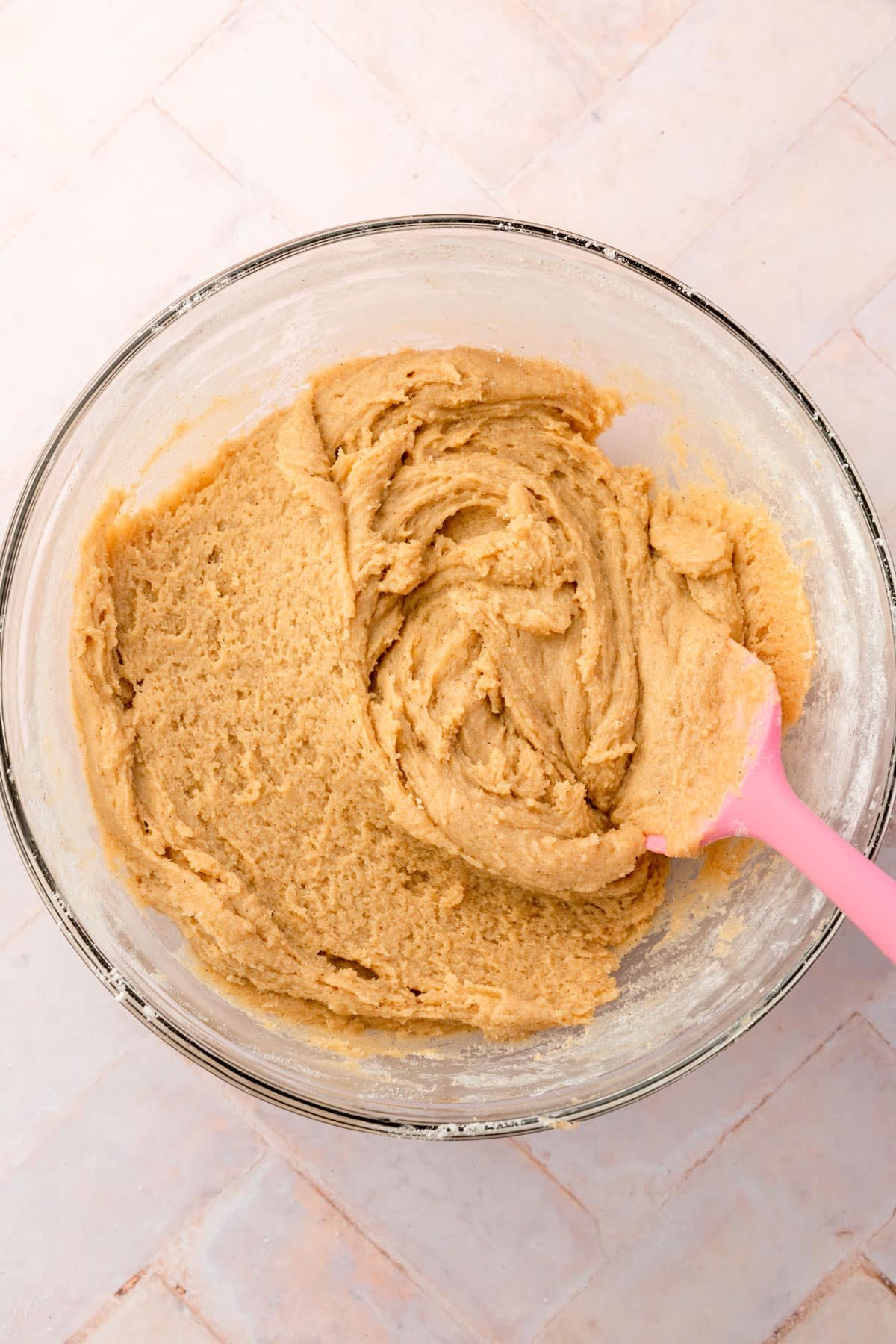 A bowl of gluten-free snickerdoodle cookie dough with a pink spatula.