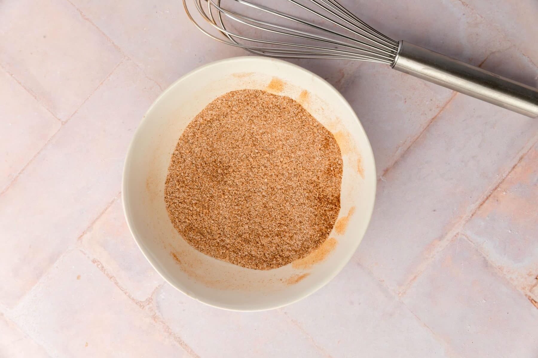 A bowl of cinnamon sugar with a whisk next to it.
