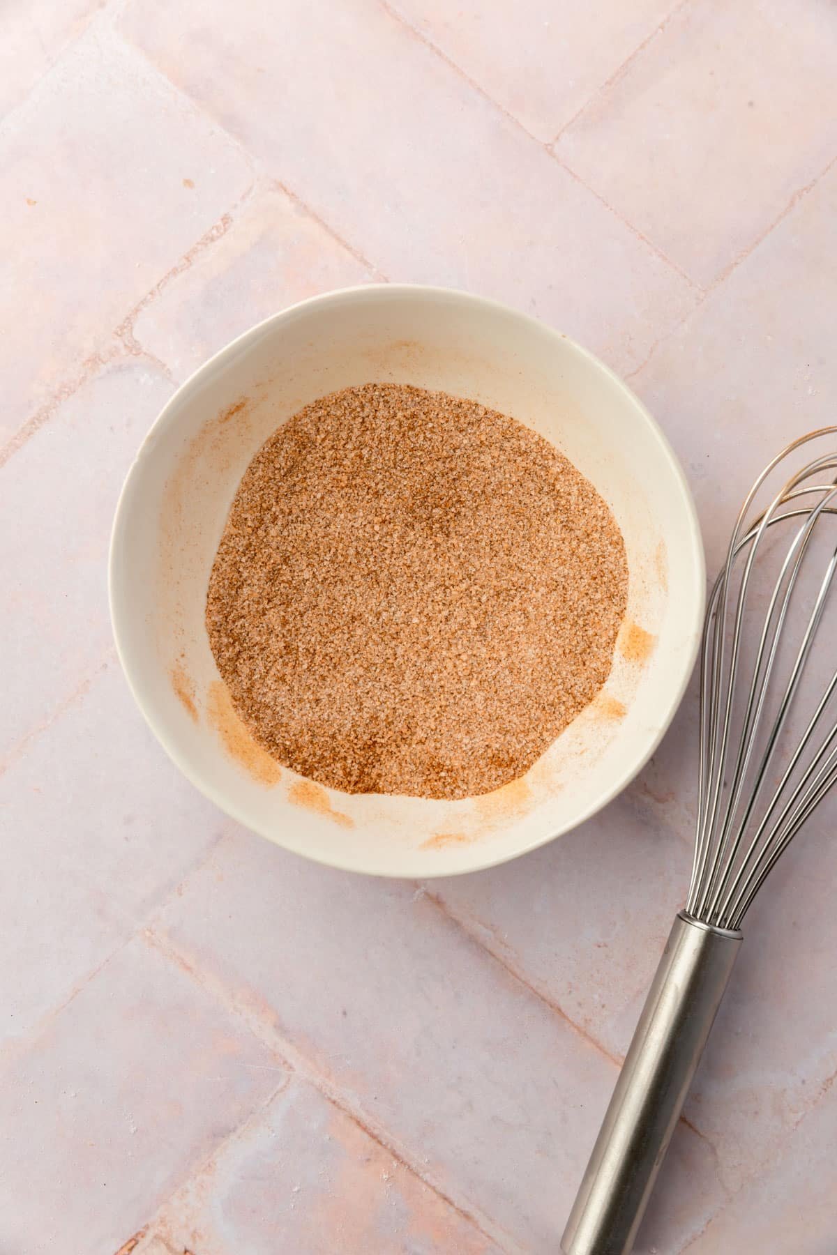 A bowl of cinnamon sugar with a whisk next to it.