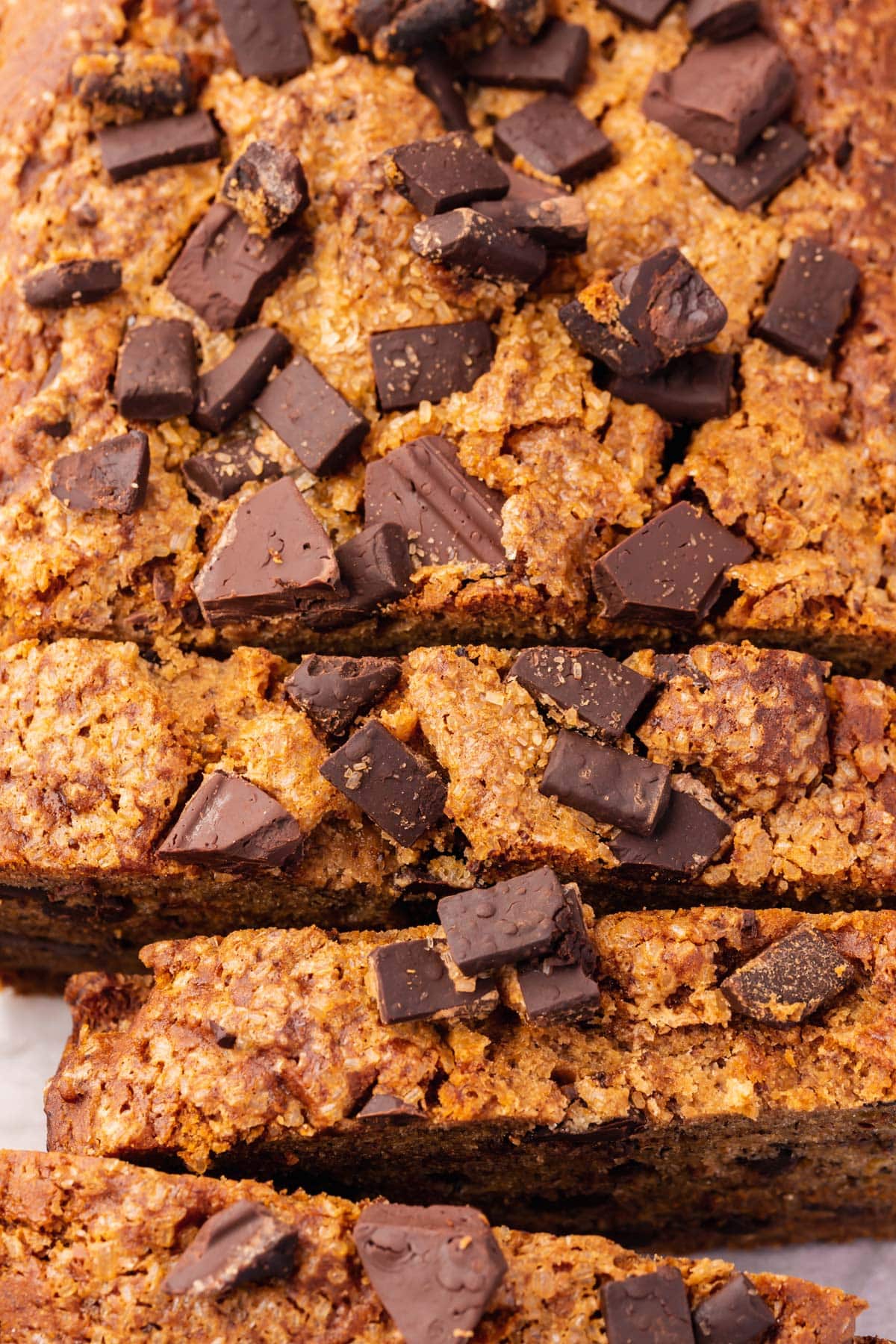 A closeup of a loaf of gluten-free vegan chocolate chunk banana bread that has been partially sliced.