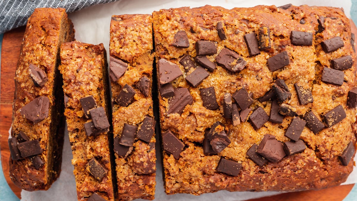 A loaf of gluten-free vegan banana bread topped with chocolate chunks that has been partially sliced.