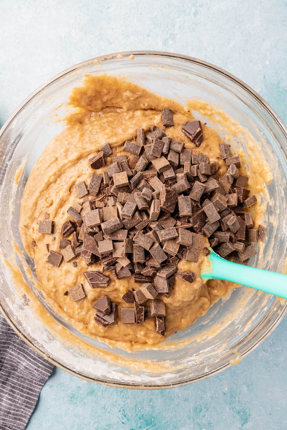 A glass mixing bowl filled with gluten-free banana bread batter that has been topped with chocolate chunks.