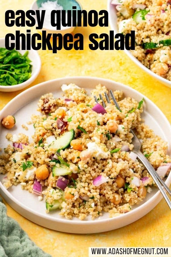 A closeup of a plate of chickpea quinoa salad with parsley, cucumber, feta, and red onion with a fork digging into the cold salad and a bowl of fresh parsley in the background.