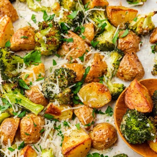 Roasted broccoli and potatoes topped with parsley and shredded parmesan cheese on a baking sheet with a wood spoon.