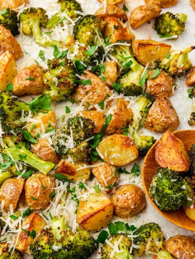 Roasted broccoli and potatoes topped with parsley and shredded parmesan cheese on a baking sheet with a wood spoon.