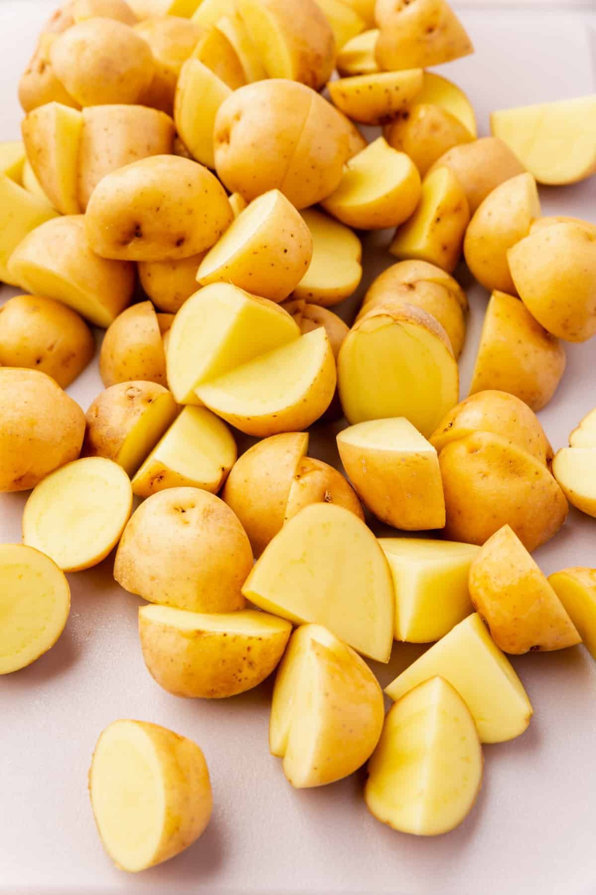 A closeup of baby yukon gold potatoes that have been sliced in half on a cutting board.
