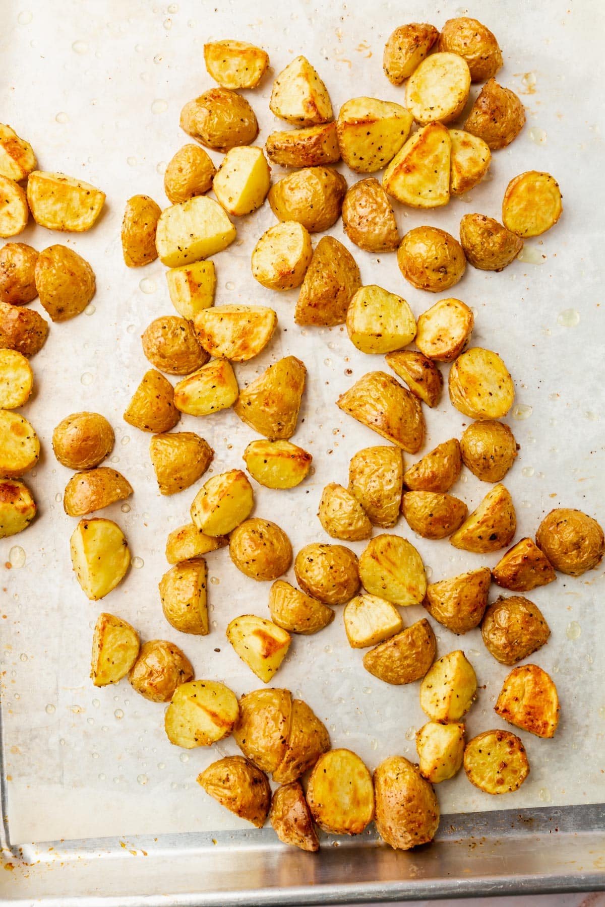 An overhead view of baby yukon gold potatoes on a baking sheet that have been roasted with oil and spices.