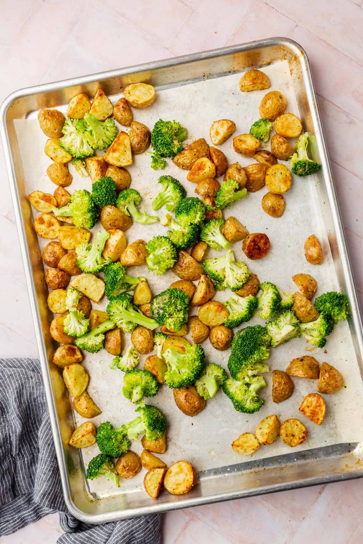 An overhead view of baby potatoes and broccoli on a baking sheet tossed together before baking.