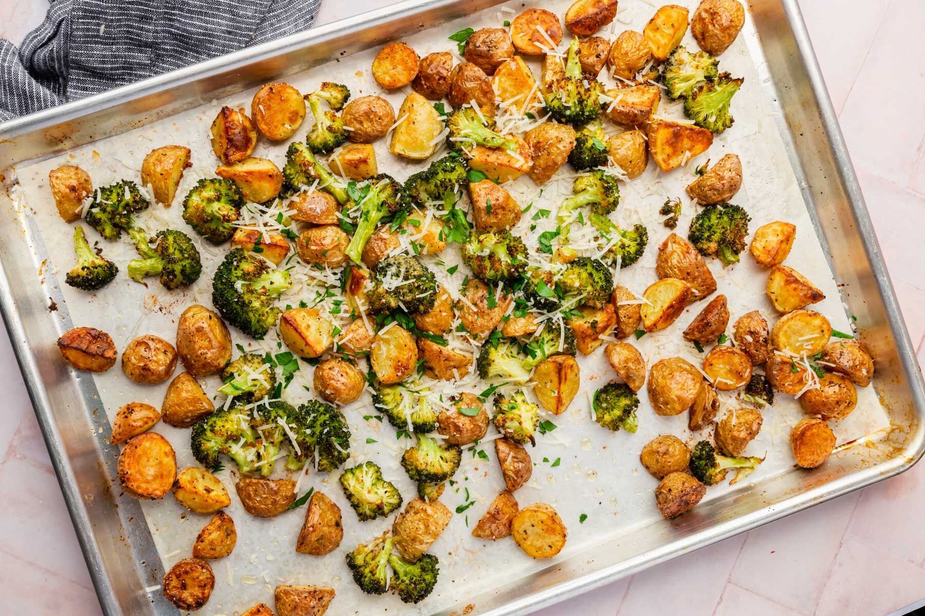 A sheet pan with roasted broccoli and potatoes topped with shredded parmesan and chopped parsley.