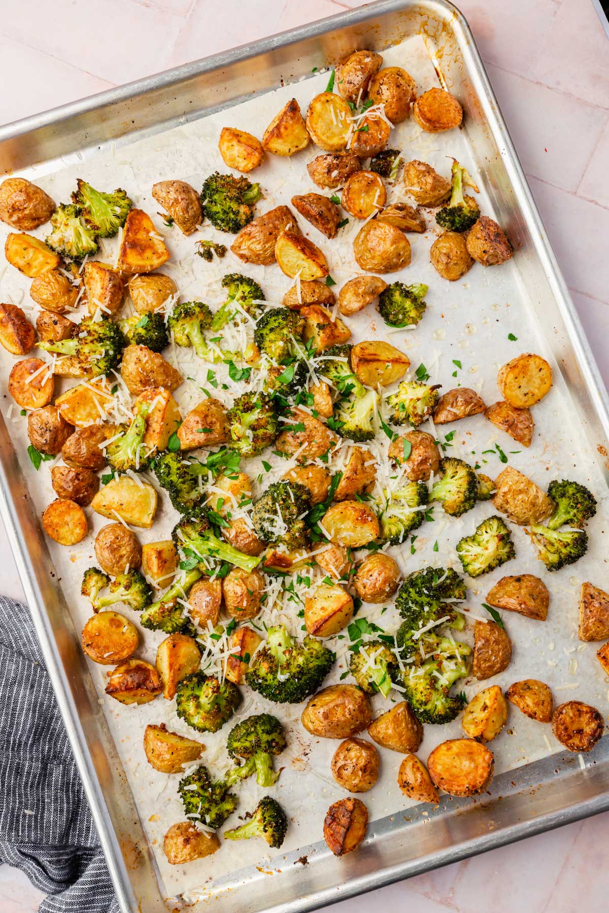 A sheet pan with roasted broccoli and potatoes topped with shredded parmesan and chopped parsley.