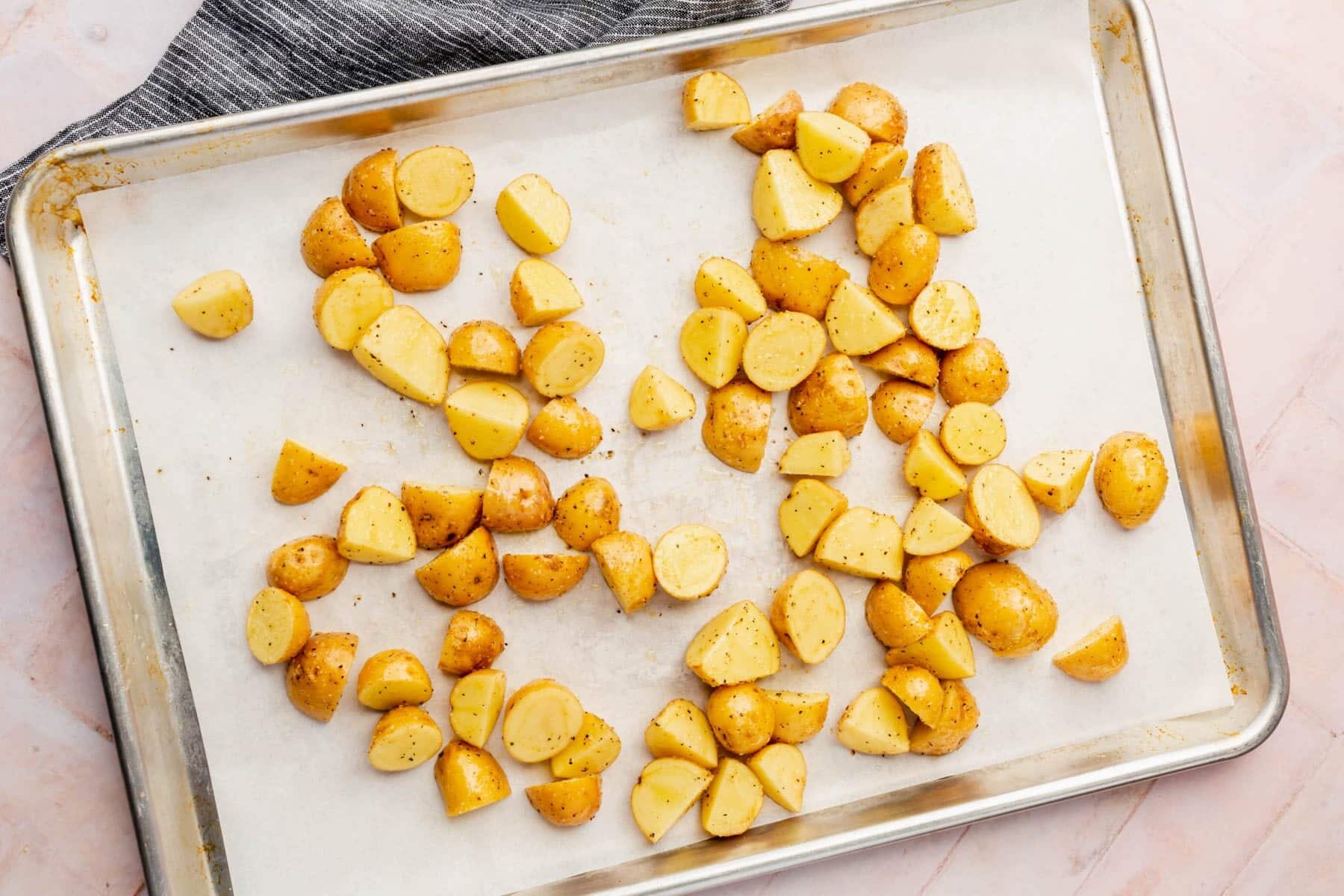 A baking sheet lined with parchment paper that has been topped with halved baby yukon gold potatoes that are tossed in oil and spices before baking.