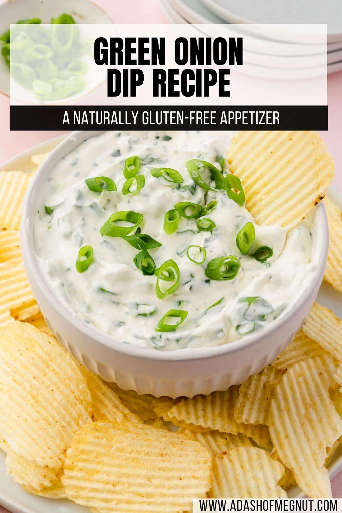 A bowl of green onion dip on a plate of potato chips with a chip in the dip.