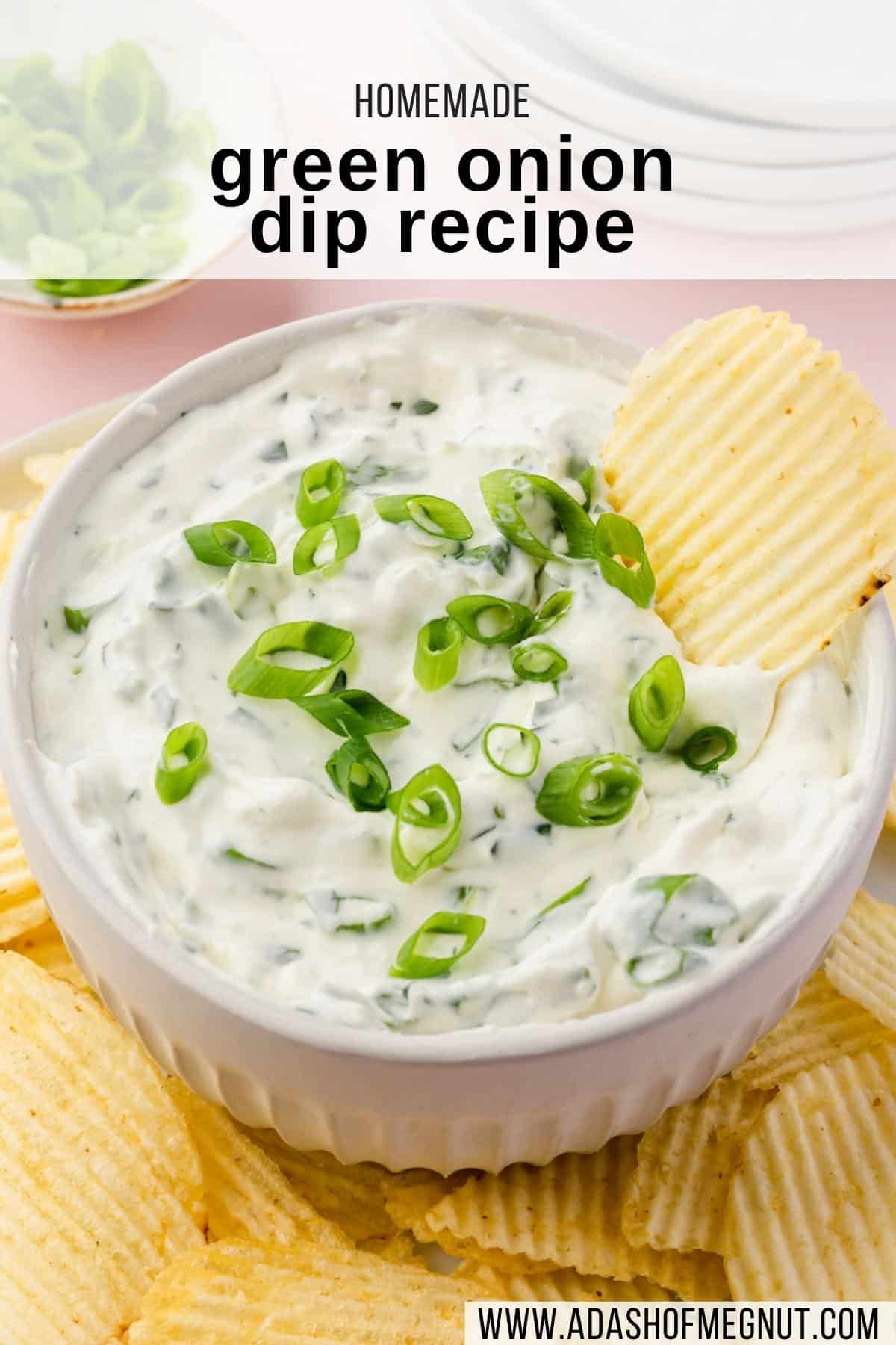 A bowl of green onion dip on a plate of potato chips with a chip in the dip.