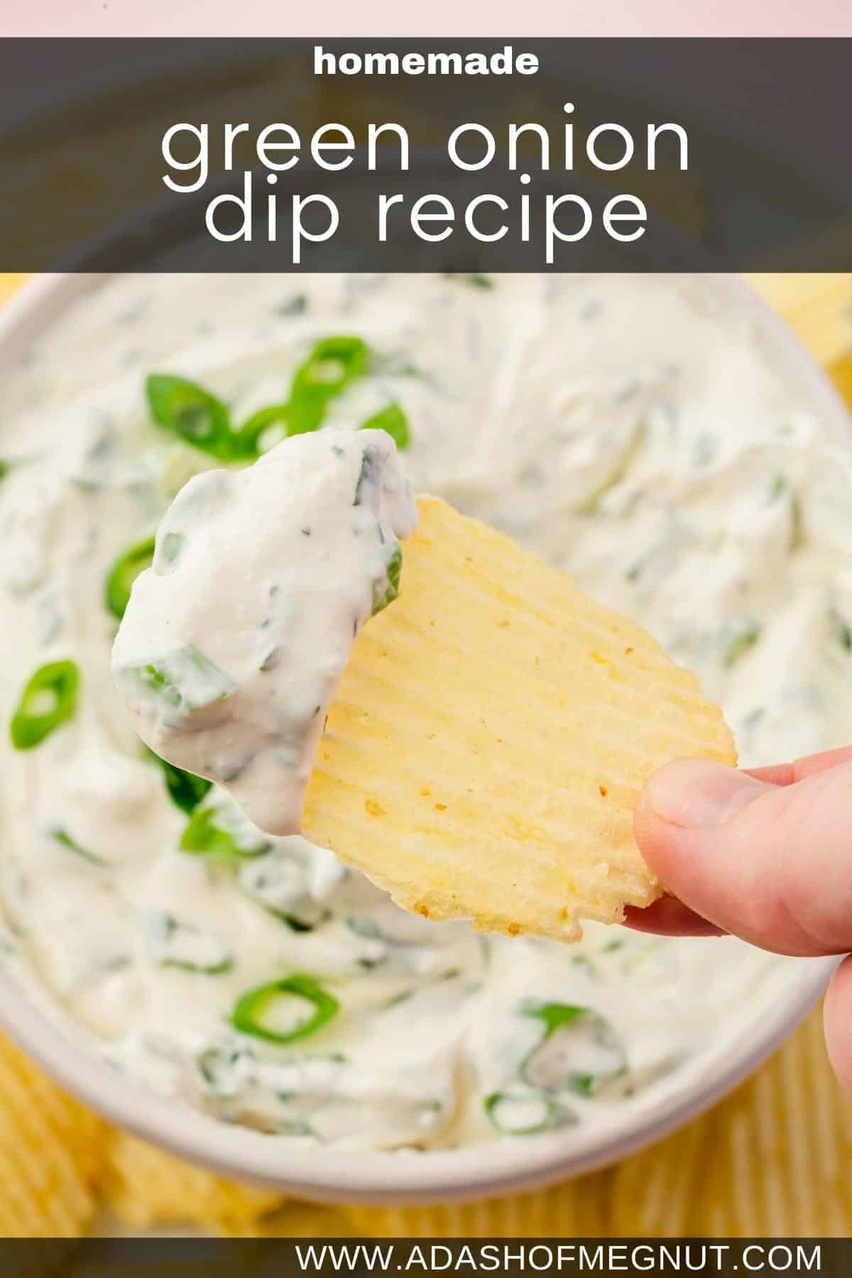A hand holding a potato chip dipped into green onion dip over a larger bowl of dip.