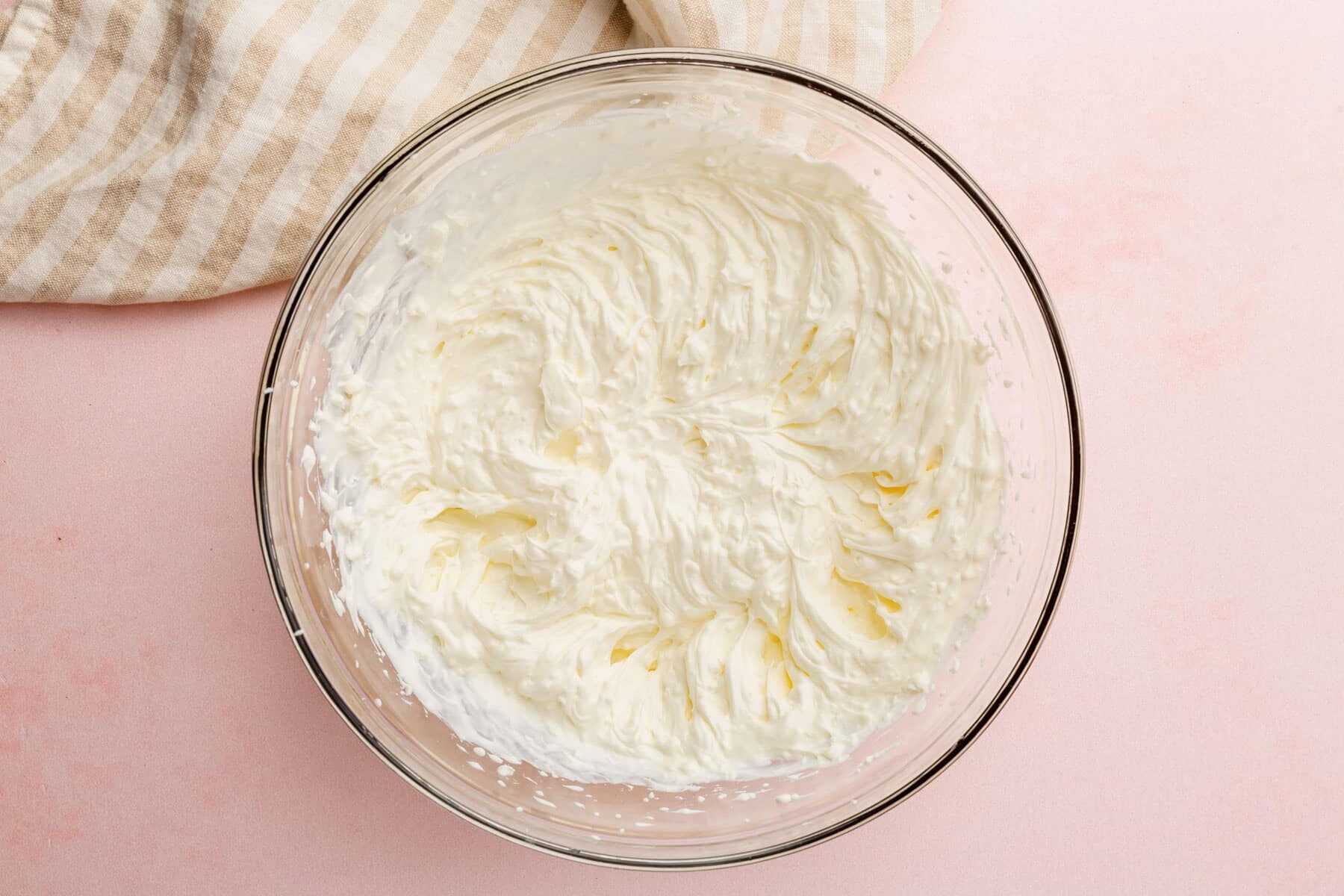 A glass mixing bowl with a cream cheese and sour cream mixture that has been blended together.