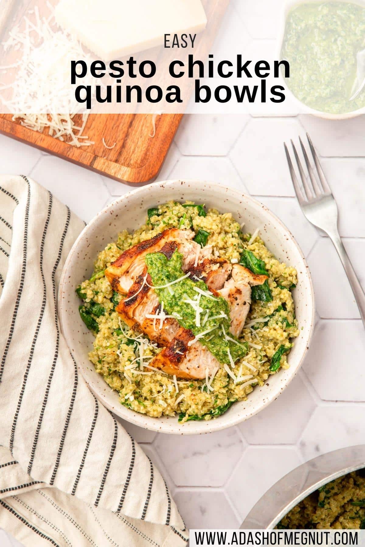 An overhead shot of a bowl of pesto quinoa topped with sliced chicken breast, pesto and shredded parmesan cheese with a fork and napkin next to it.