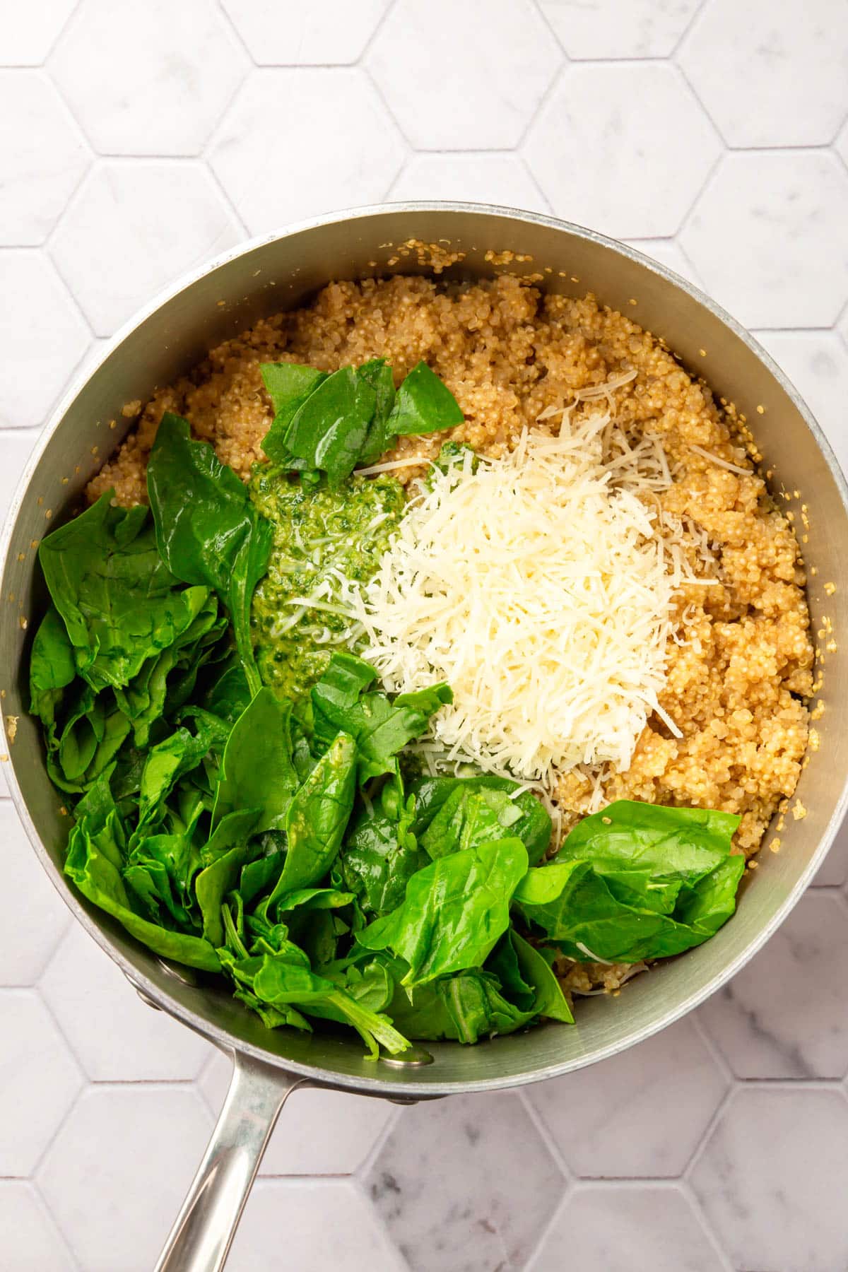 A stainless steel pot filled with quinoa, shredded parmesan cheese, spinach and pesto before mixing together.