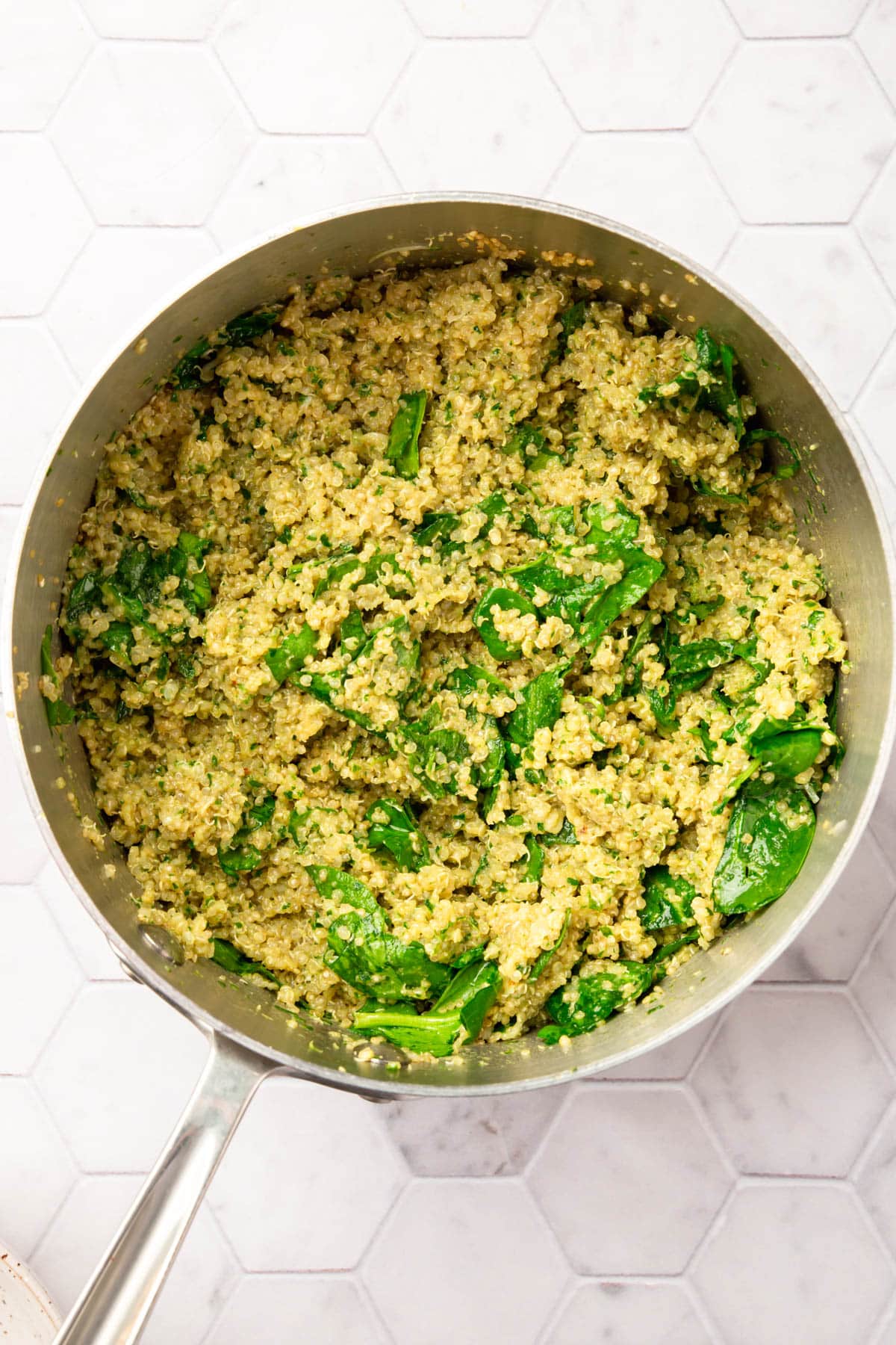 A stainless steel pot filled with quinoa mixed with spinach and pesto.