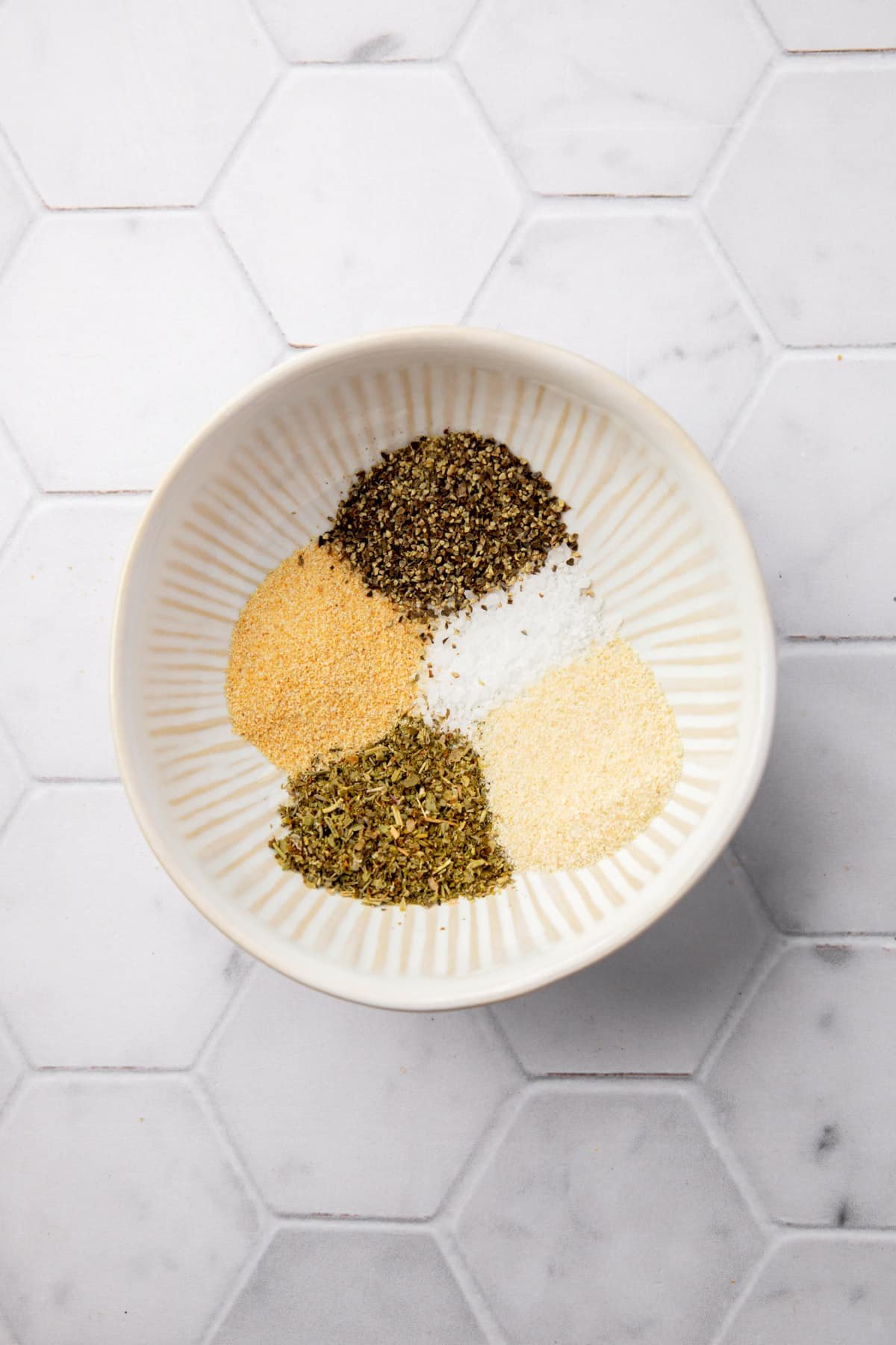 A small bowl with garlic powder, black pepper, salt, onion powder, and Italian herb seasoning blend before mixing together.