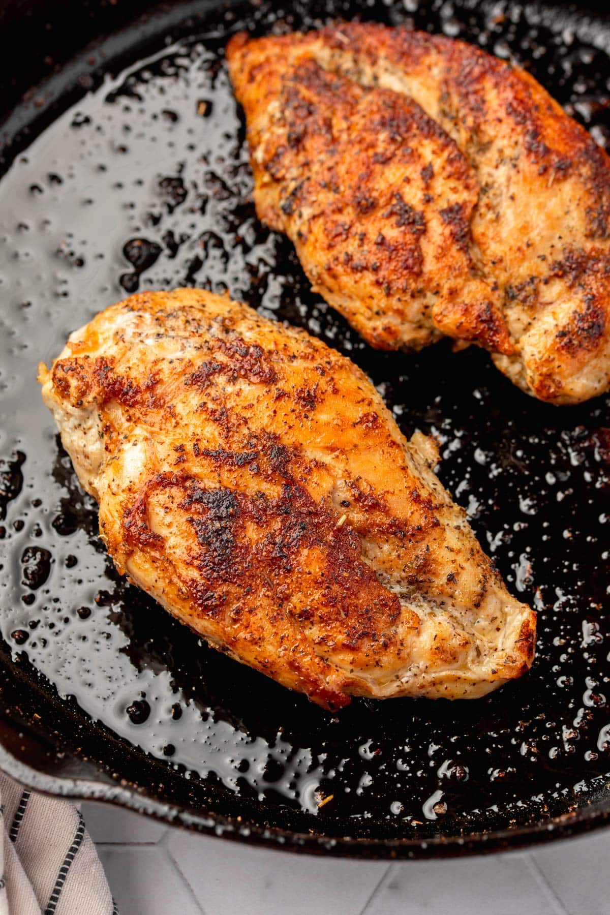 Two cooked chicken breasts in a cast iron skillet.