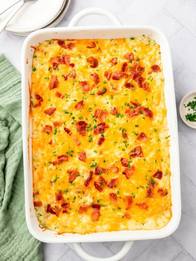 A casserole dish of twice baked mashed potatoes topped with bacon bits, chopped chives and melted cheddar cheese.