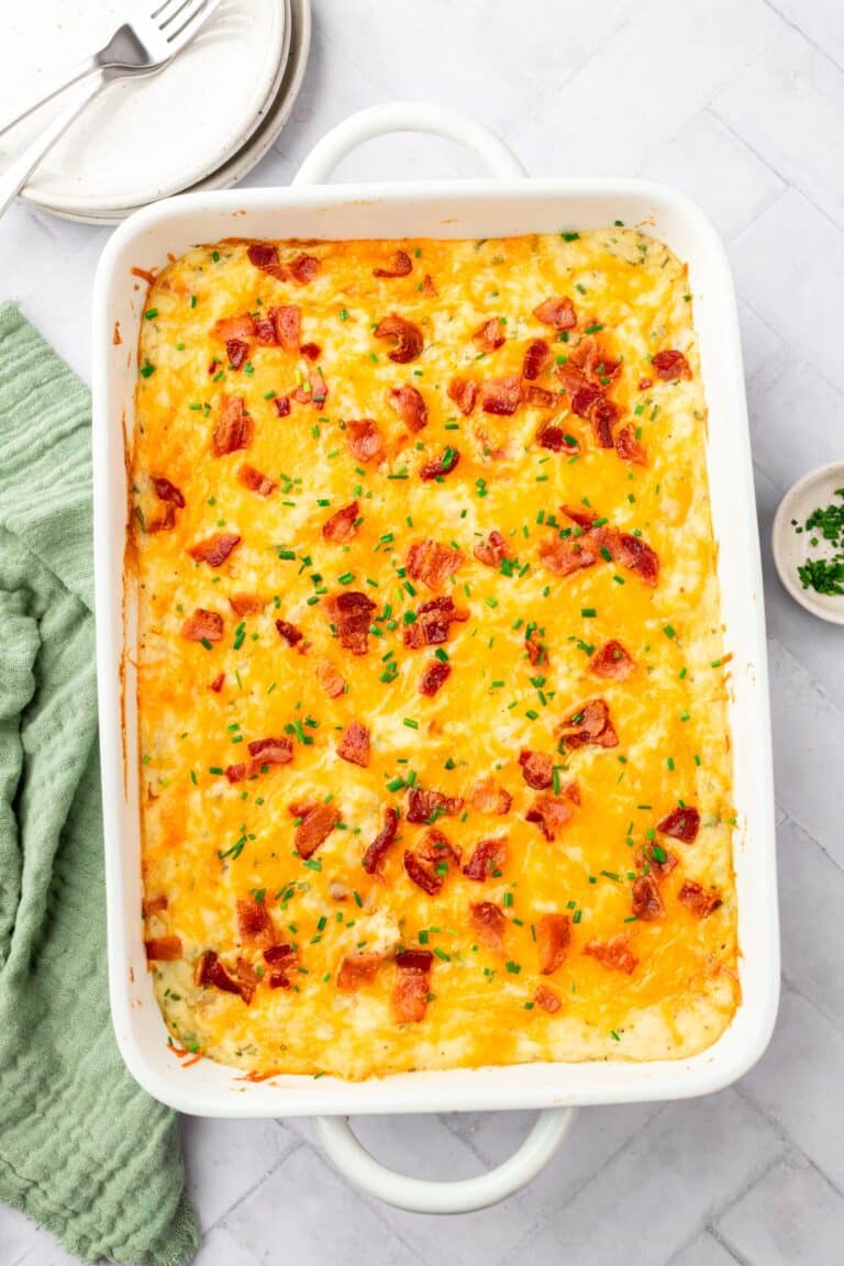 A casserole dish of twice baked mashed potatoes topped with bacon bits, chopped chives and melted cheddar cheese.