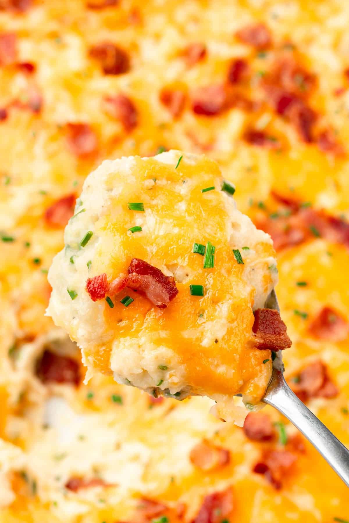 A large spoonful of twice baked mashed potatoes over a larger casserole dish.