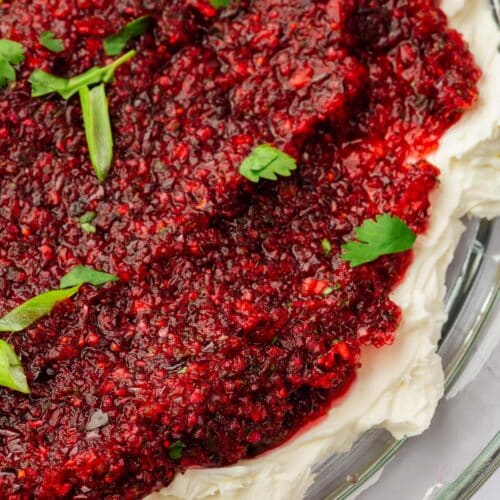 A close up of cranberry cream cheese dip on a platter with a bottom layer of cream cheese topped with cranberry jalapeño salsa, diced green onion and chopped cilantro.