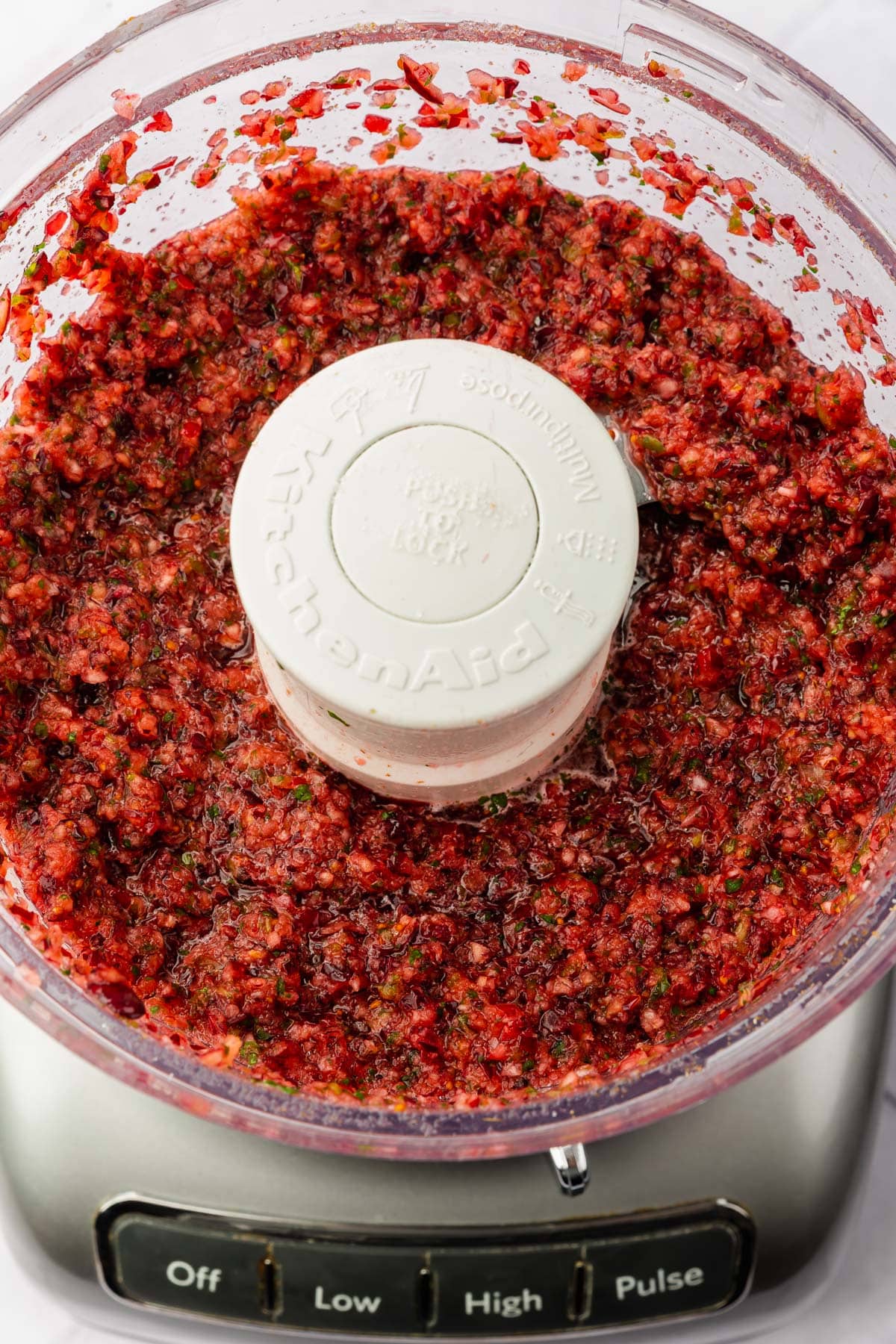 A food processor with cranberry jalapeño salsa in it that has been pulsed until finely chopped.