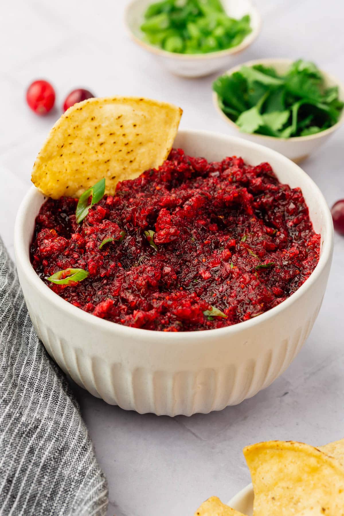 A bowl of cranberry salsa topped with green onion with a tortilla chip in it.