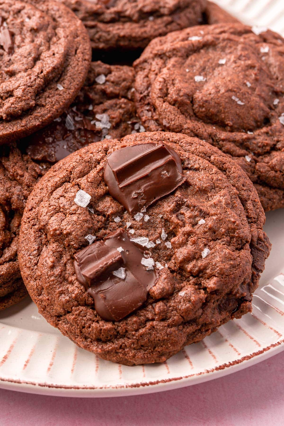 A closeup of a pile of gluten-free chocolate chunk cookies topped with flaky Maldon salt.