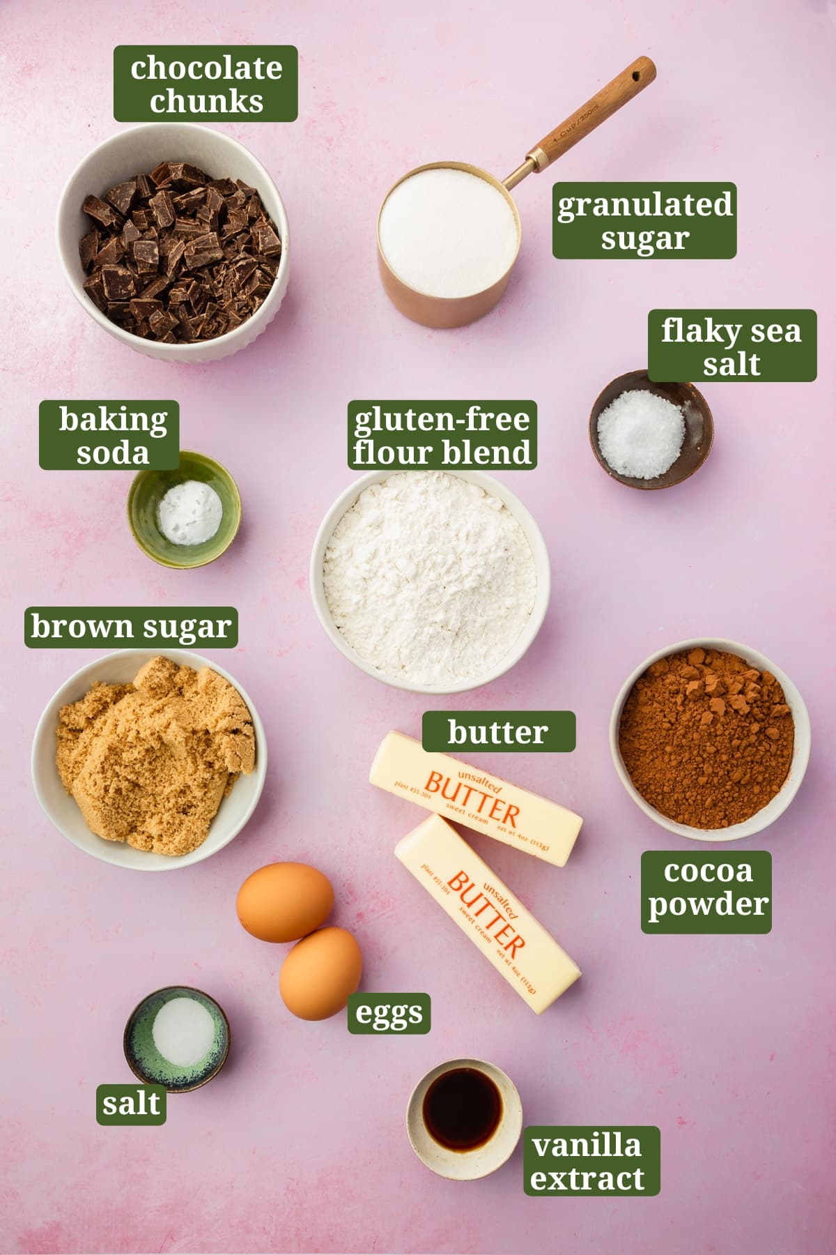 Small bowls of ingredients on a pink table to make gluten-free chocolate cookies, including chopped chocolate, gluten-free flour blend, cocoa powder, brown sugar, granulated sugar, butter, eggs, vanilla, baking soda, and salt with text overlays over each ingredient.