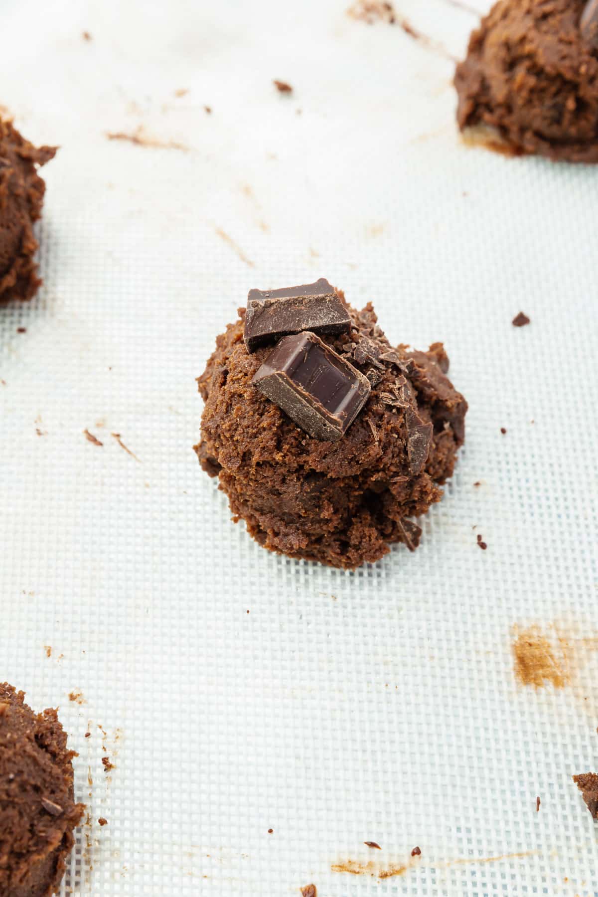 A close up of a gluten-free chocolate cookie dough ball topped with two chunks of chopped chocolate.