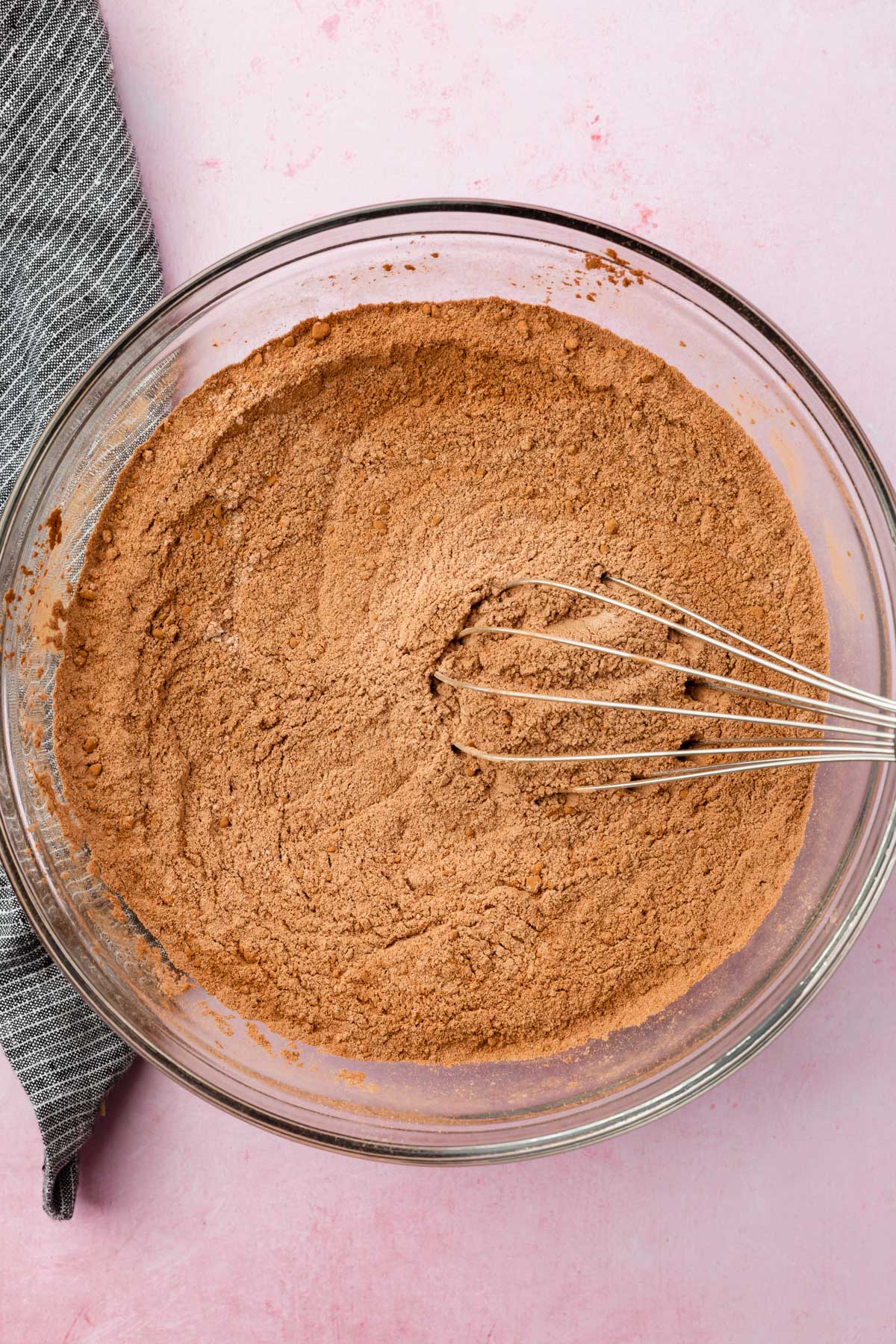 A glass mixing bowl with cocoa powder and flour mixture with a whisk in it.