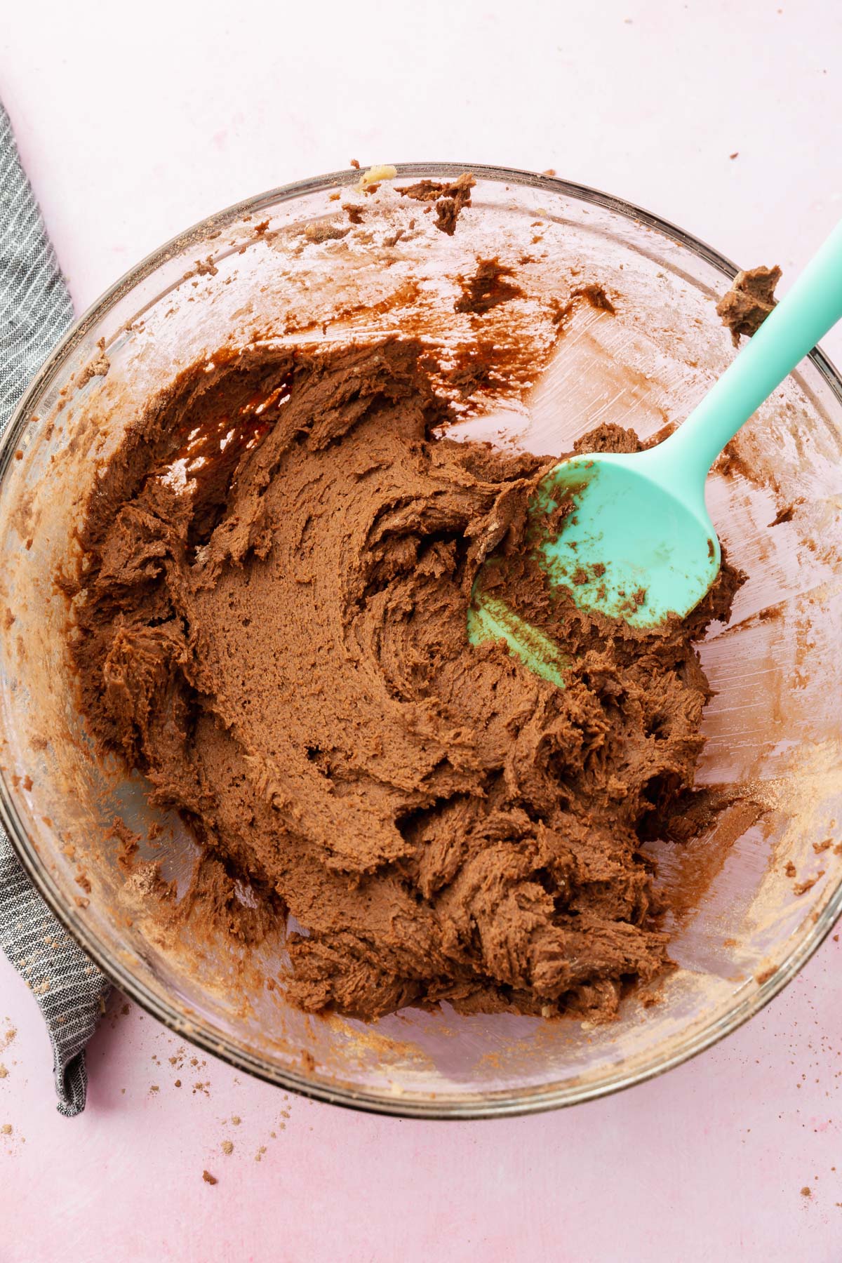 A gluten-free chocolate cookie dough in a glass mixing bowl with a blue spatula.