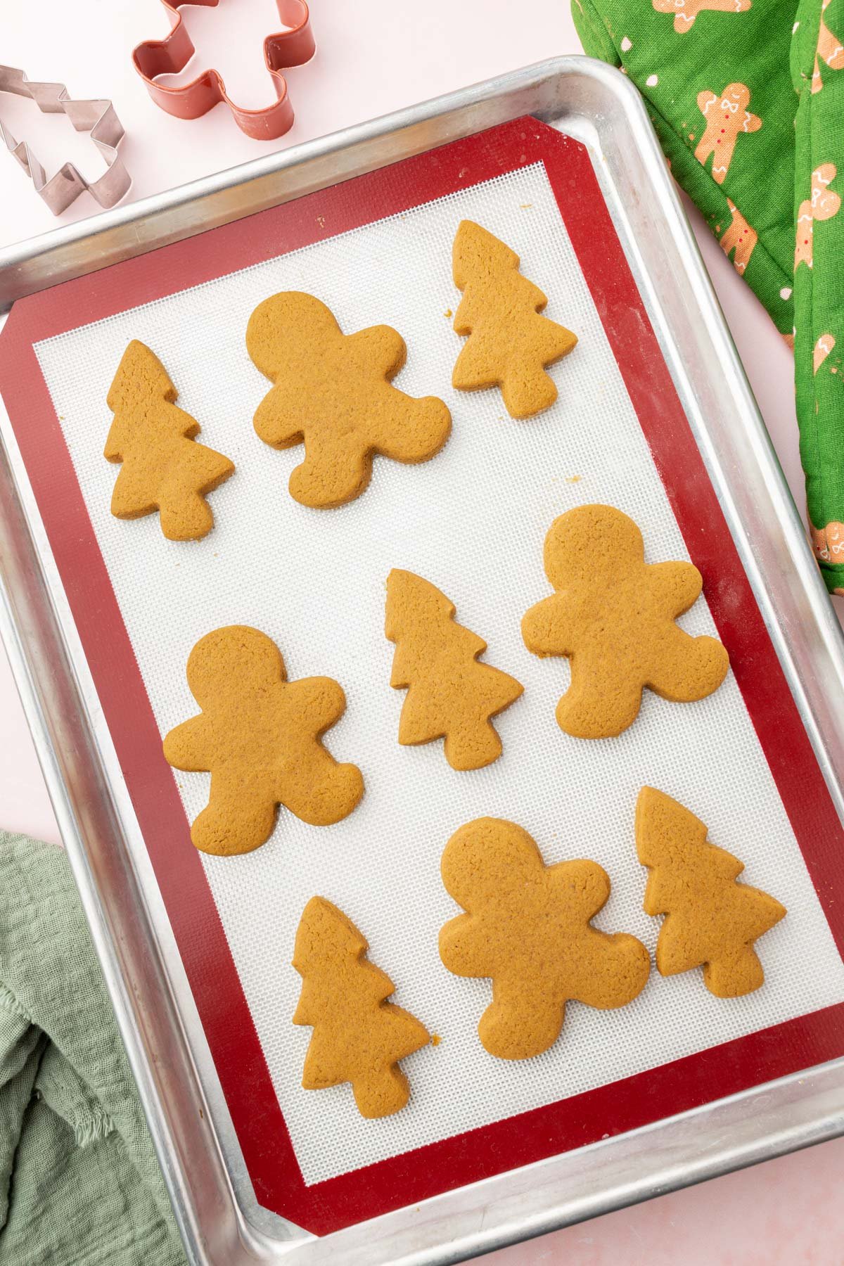 A baking sheet lined with a silicone baking mat with gluten-free gingerbread men and gingerbread Christmas tree cookies on it.
