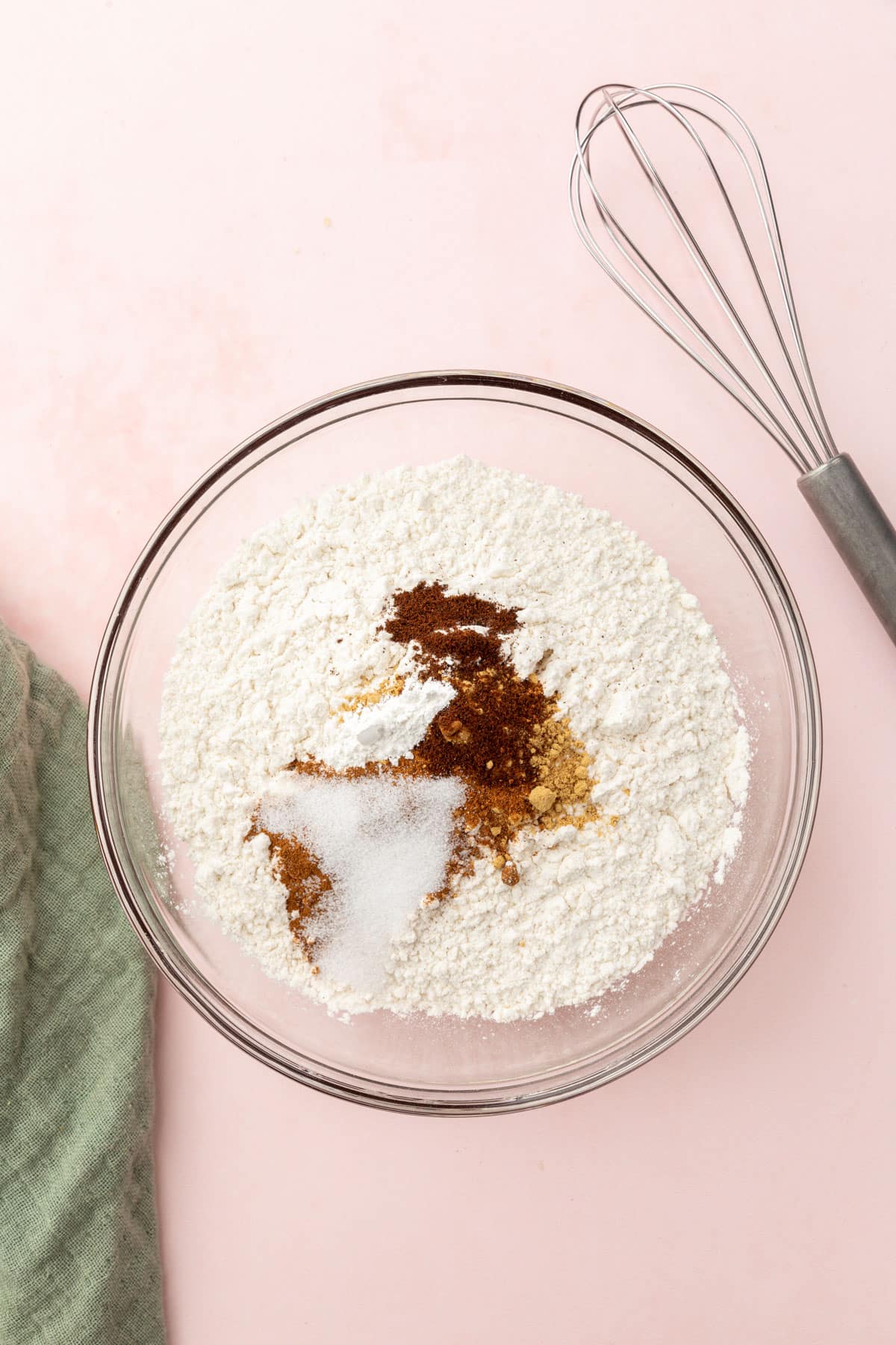A glass mixing bowl with gluten-free flour, cinnamon, nutmeg, cloves, ginger, baking powder and salt before mixing together.