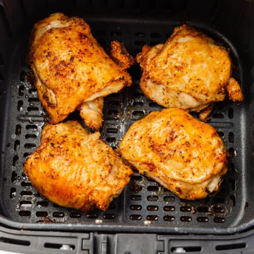 Four crispy bone-in chicken thighs in an air fryer basket after cooking.