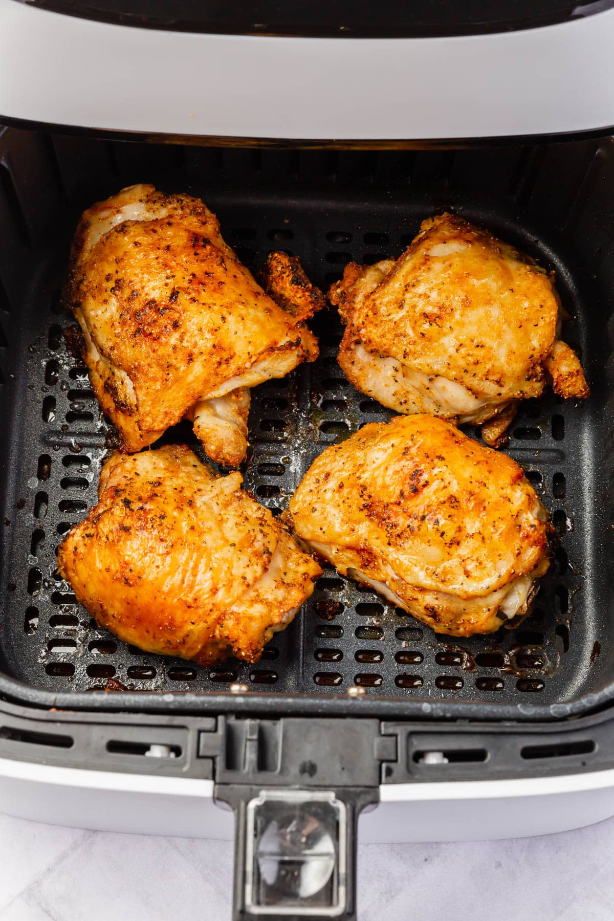 Four crispy bone-in chicken thighs in an air fryer basket after cooking.