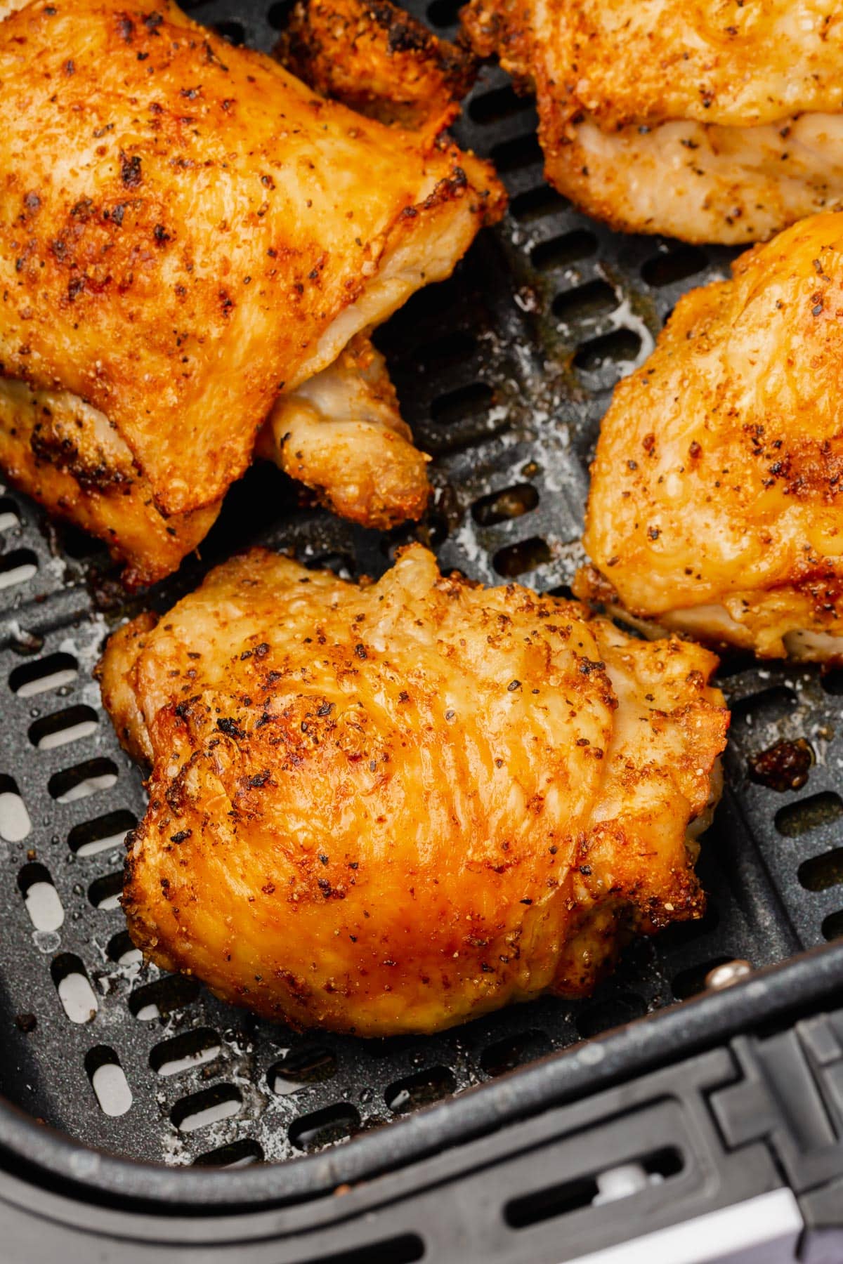 A closeup of crispy bone-in chicken thighs with skin in the air fryer basket.