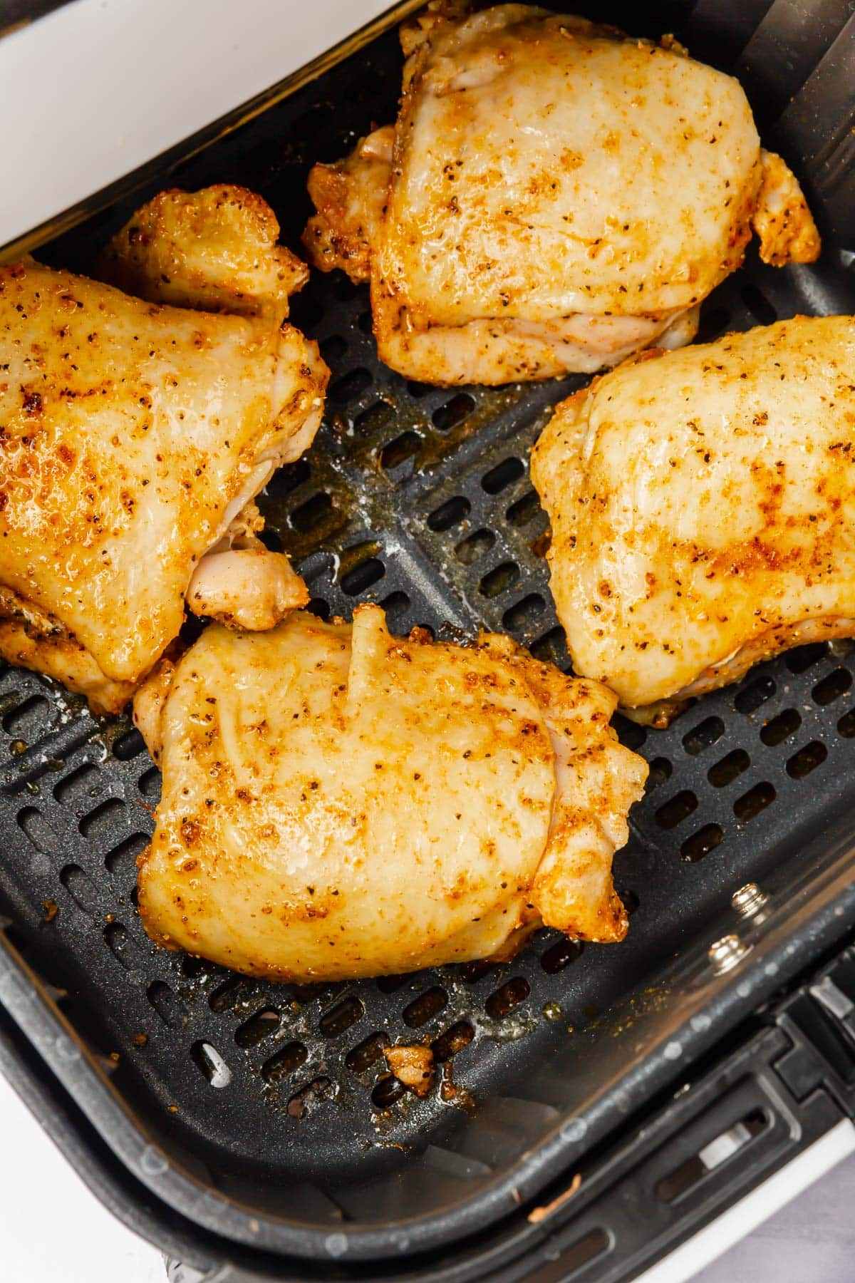 Partially cooked seasoned chicken thighs with skin in an air fryer basket.