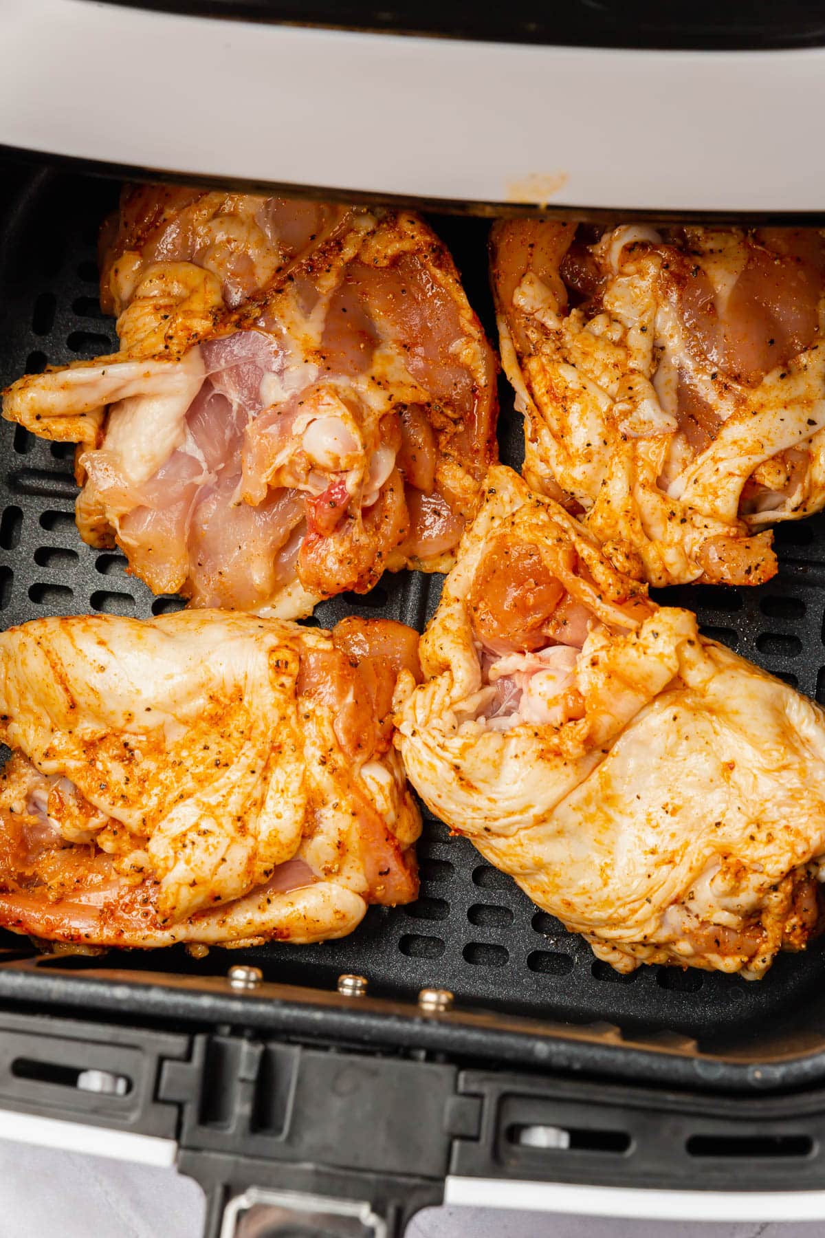 Raw chicken thighs in an air fryer basket with the skin side down.