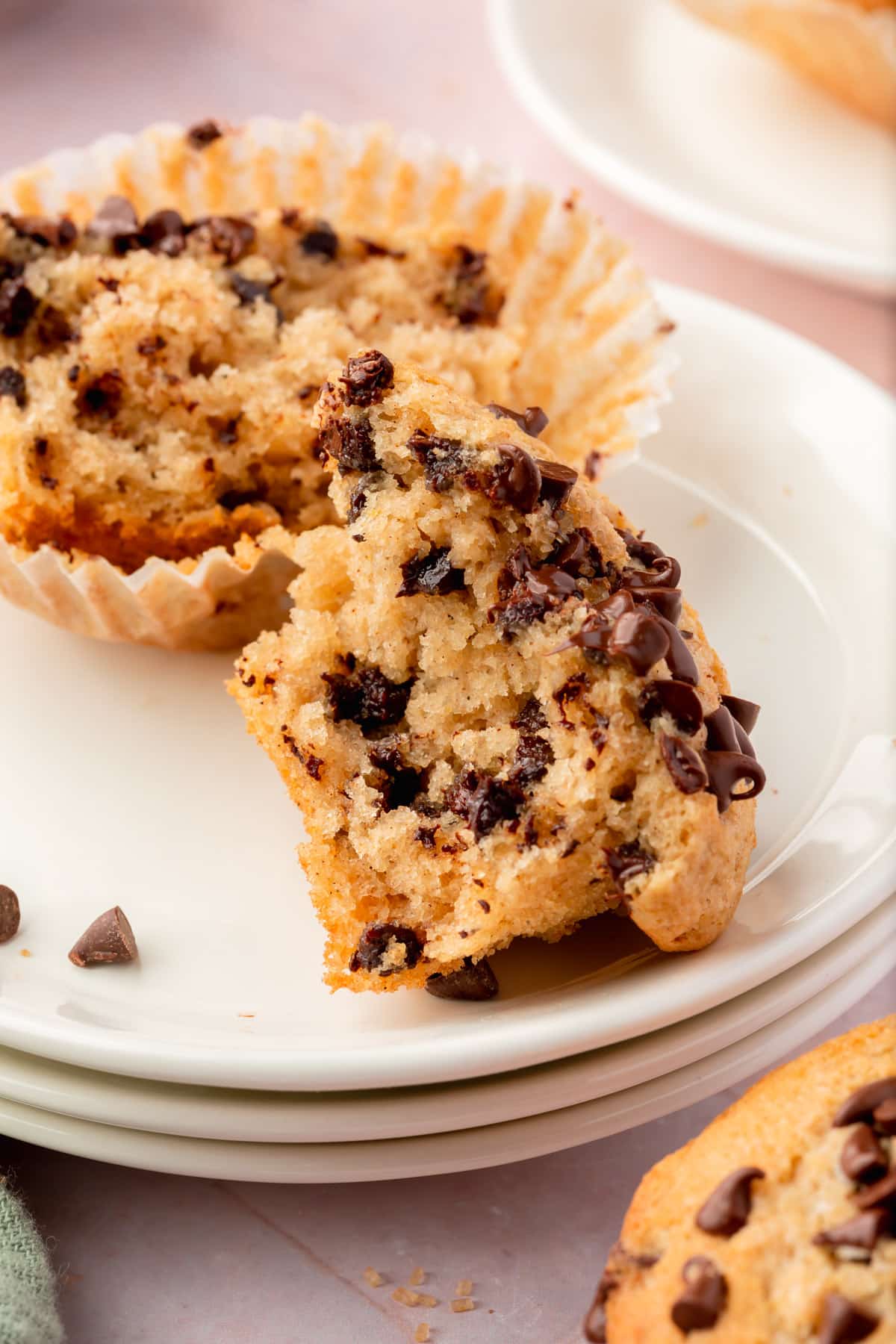 A close up of a gluten-free chocolate chip muffin that has been broken in half to show the fluffy inside on a stack of dessert plates.