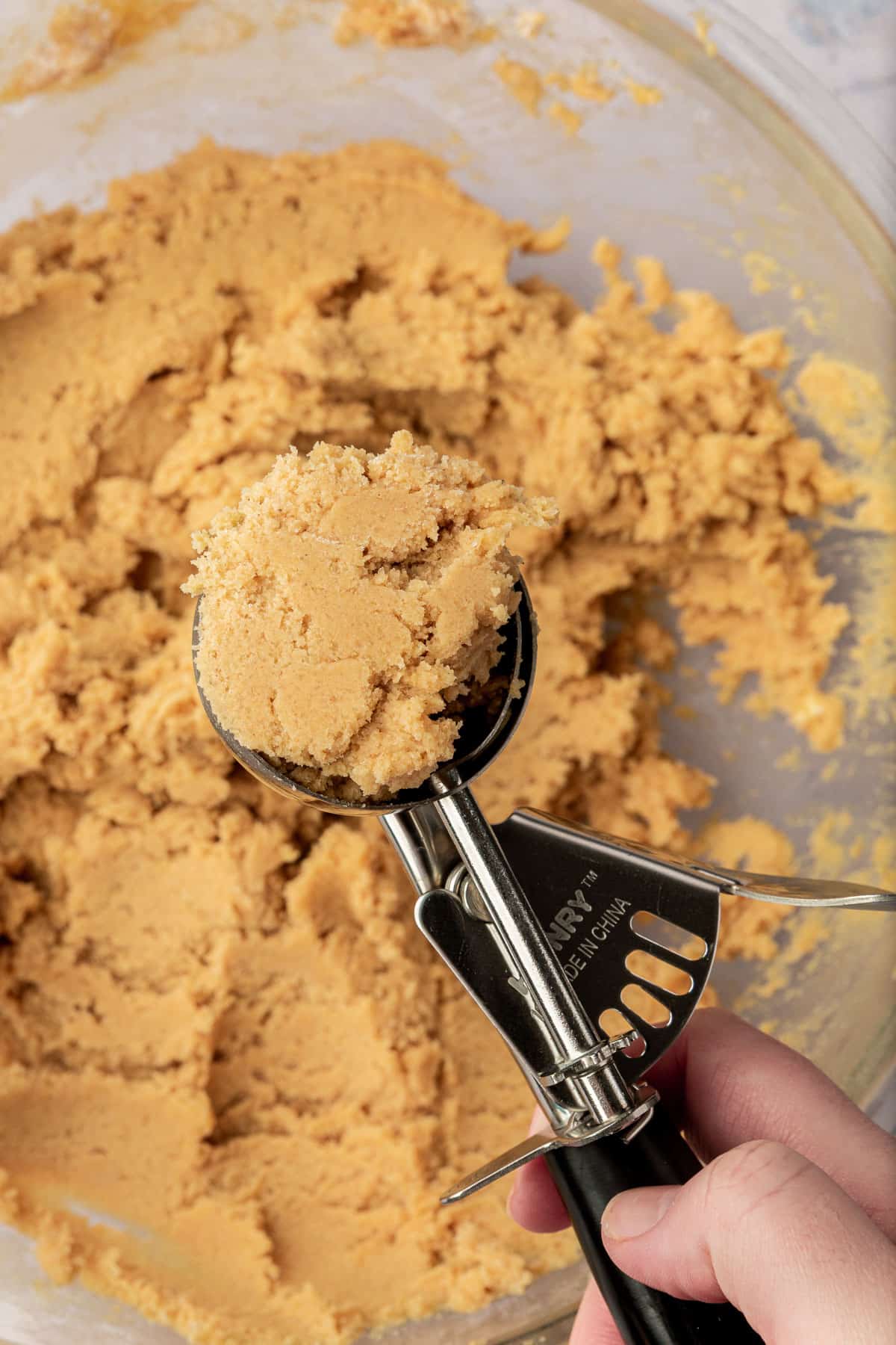 A cookie scoop with snickerdoodle cookie dough in it over a large bowl of gluten-free cookie dough.