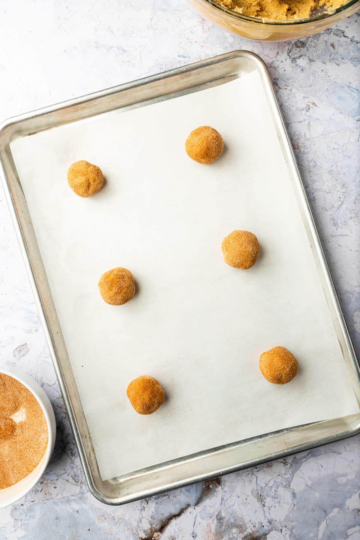 Six gluten-free snickerdoodle cookie dough balls on a baking sheet lined with parchment paper before baking in the oven.