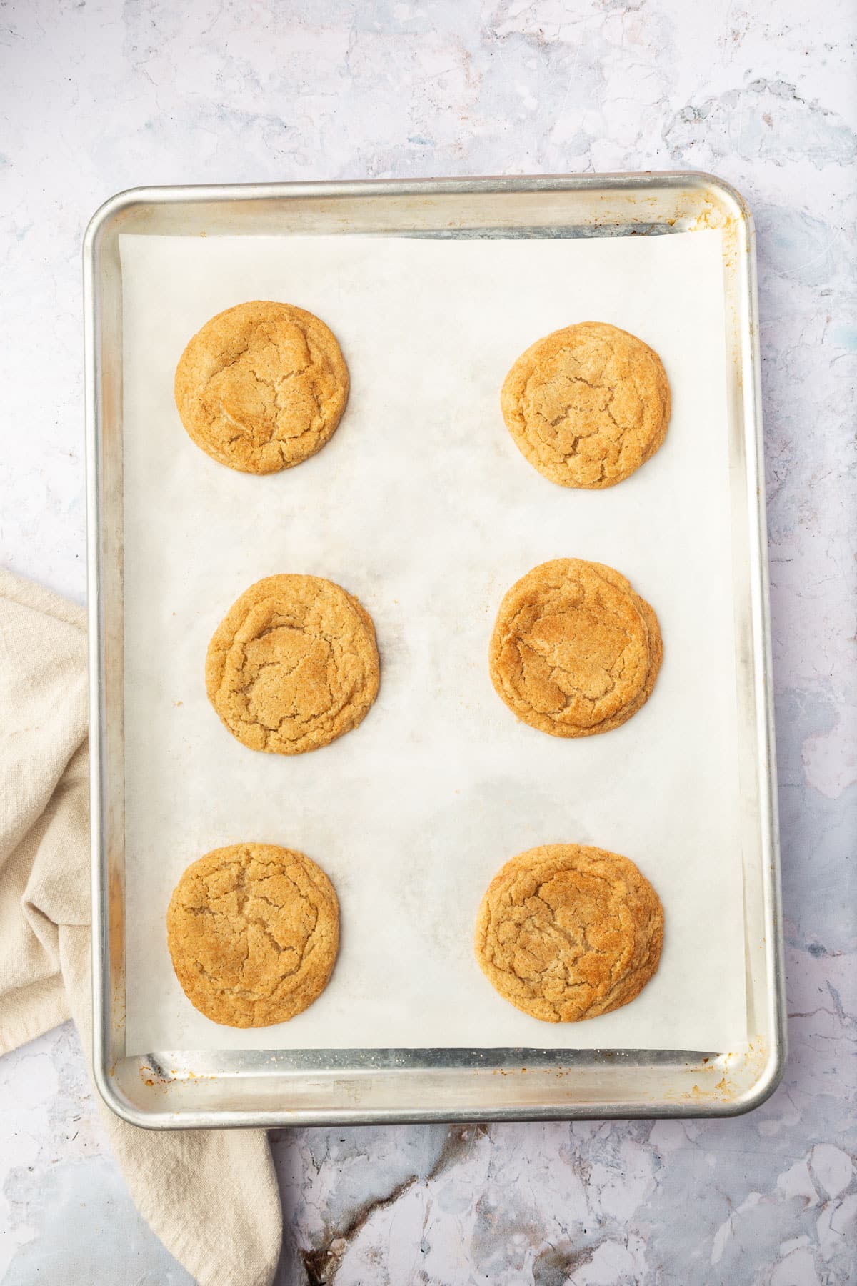 Six snickerdoodle cookies on a sheet pan lined with parchment paper.