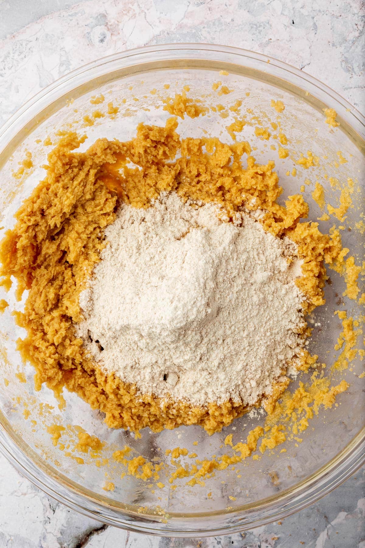 Gluten-free flour on top of a butter and sugar mixture to make cookies in a glass mixing bowl.